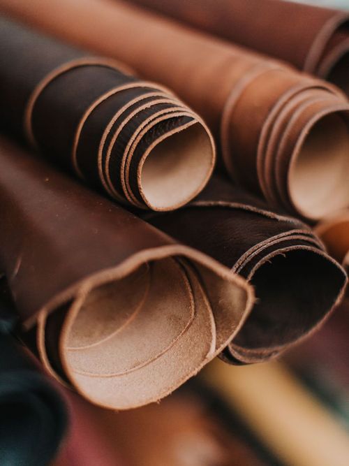Rollos de cuero curtido en tonos tabaco y chocolate apilados con luz suave