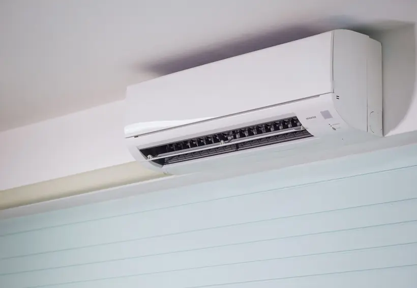 Aire acondicionado tipo split blanco instalado en la parte alta de una pared clara
