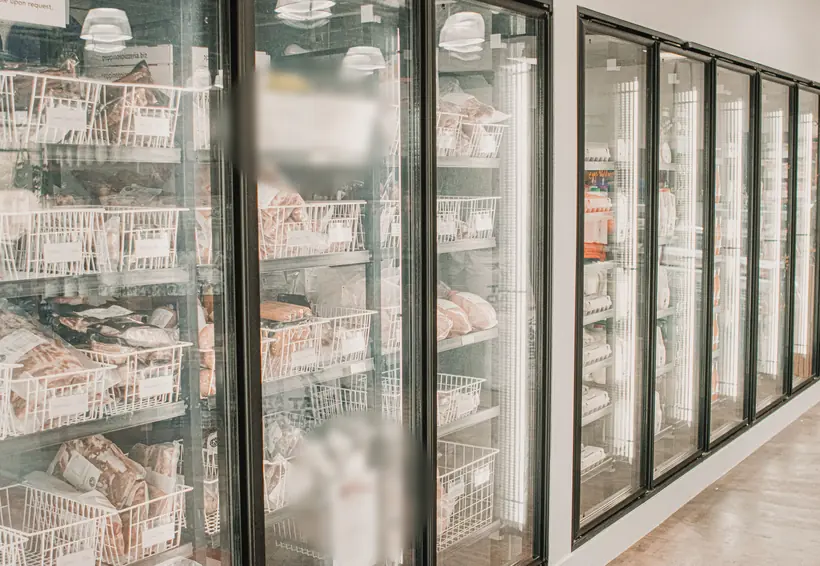 Fila de freezers verticales de puerta de cristal con canastas de productos congelados