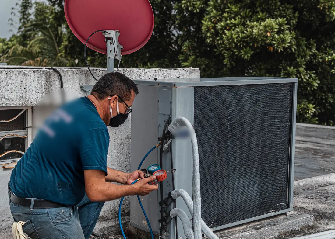 Técnico con manómetros de refrigerante midiendo la carga de un equipo de refrigeración en una azotea