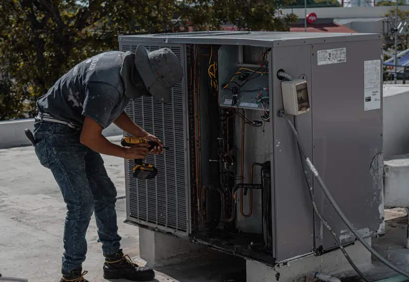 Técnico con taladro trabajando sobre una unidad de climatización abierta en una azotea