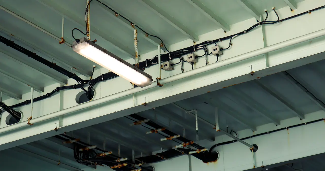Canalizaciones y luminaria industrial montadas sobre la estructura metálica del techo de una nave