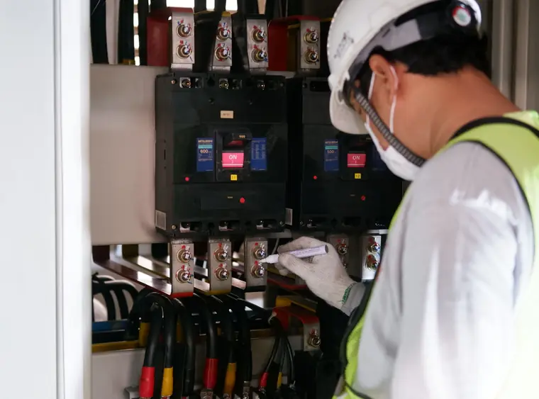 Técnico con casco y chaleco reflectivo revisando las protecciones de un tablero eléctrico