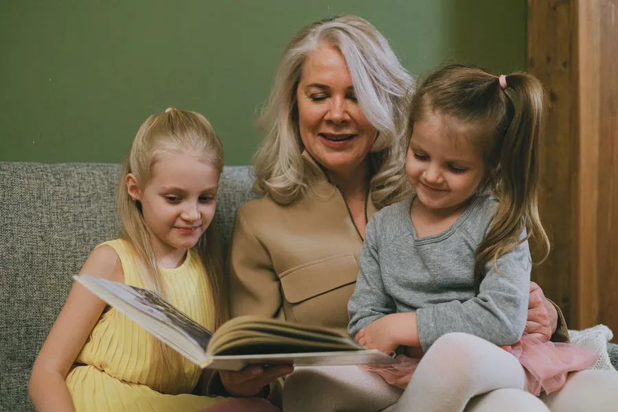 An adult and two young children sitting together reading a picture book in a warm, softly lit room