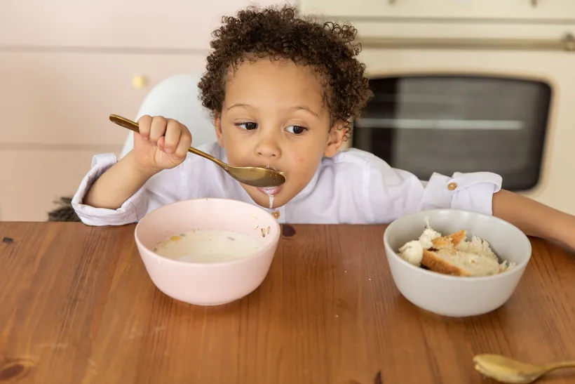 A young child eating a bowl of cereal at a wooden kitchen table at home