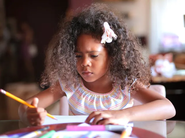 A school-age child concentrating while writing with a pencil at a table