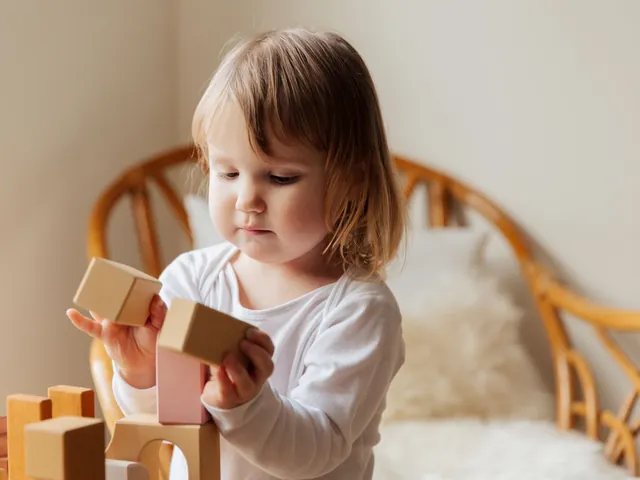 A toddler standing and stacking wooden blocks in a bright room