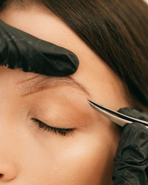 Esteticista con guantes perfilando la ceja de una clienta tumbada
