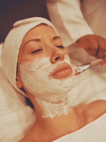 Clienta con una mascarilla facial blanca que le aplican con pincel, con el pelo recogido en una toalla