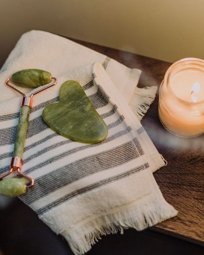 Rodillo y gua sha de jade sobre una toalla de rayas, junto a una vela encendida