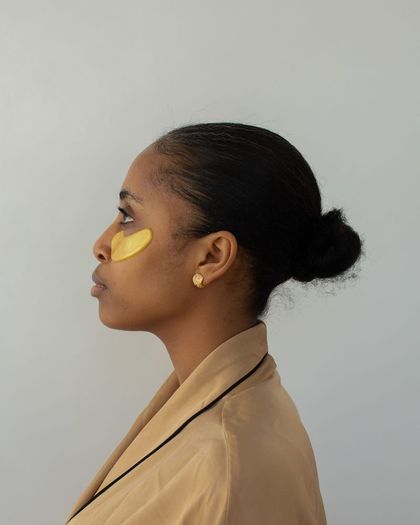 Mujer de perfil con parches dorados bajo los ojos y el pelo recogido