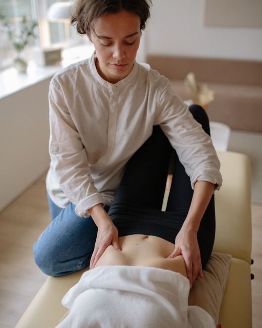 Terapeuta trabajando el abdomen cubierto de una clienta en camilla
